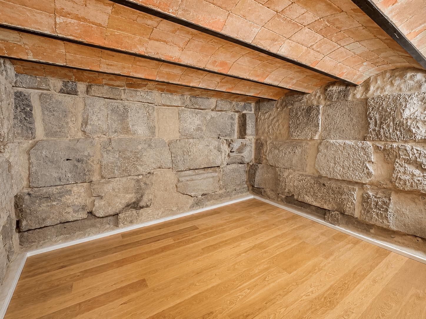Habitación vacía con dos paredes de sillería de piedra, bóveda de ladrillo y suelo de roble recién puesto.