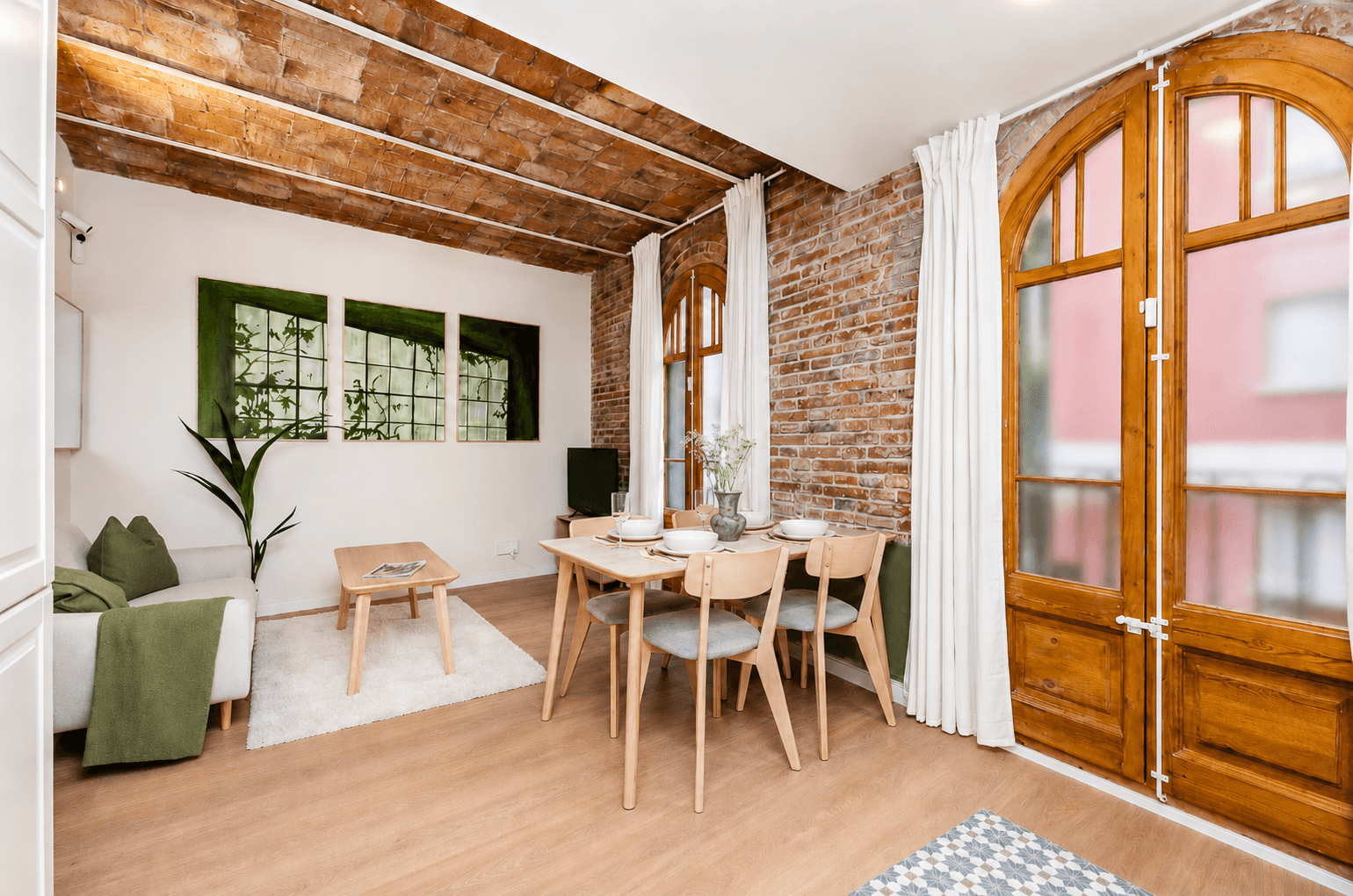 Salón comedor con bóveda de ladrillo, sofá claro, mesa de madera y dos balconeras de arco con cortinas blancas.