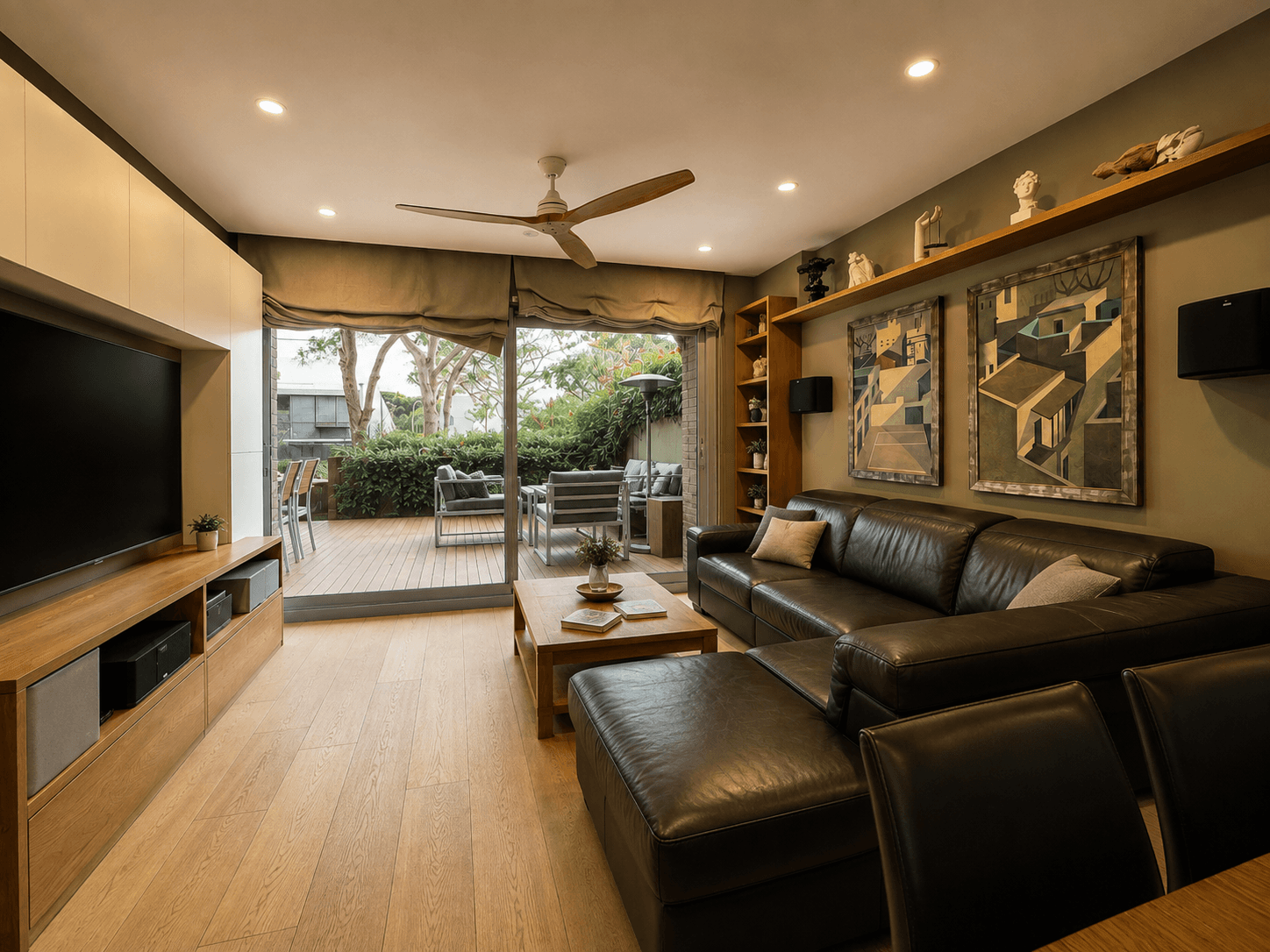 Salón con sofá de piel, mueble bajo de roble y ventanal corredero abierto a una terraza de madera con árboles.