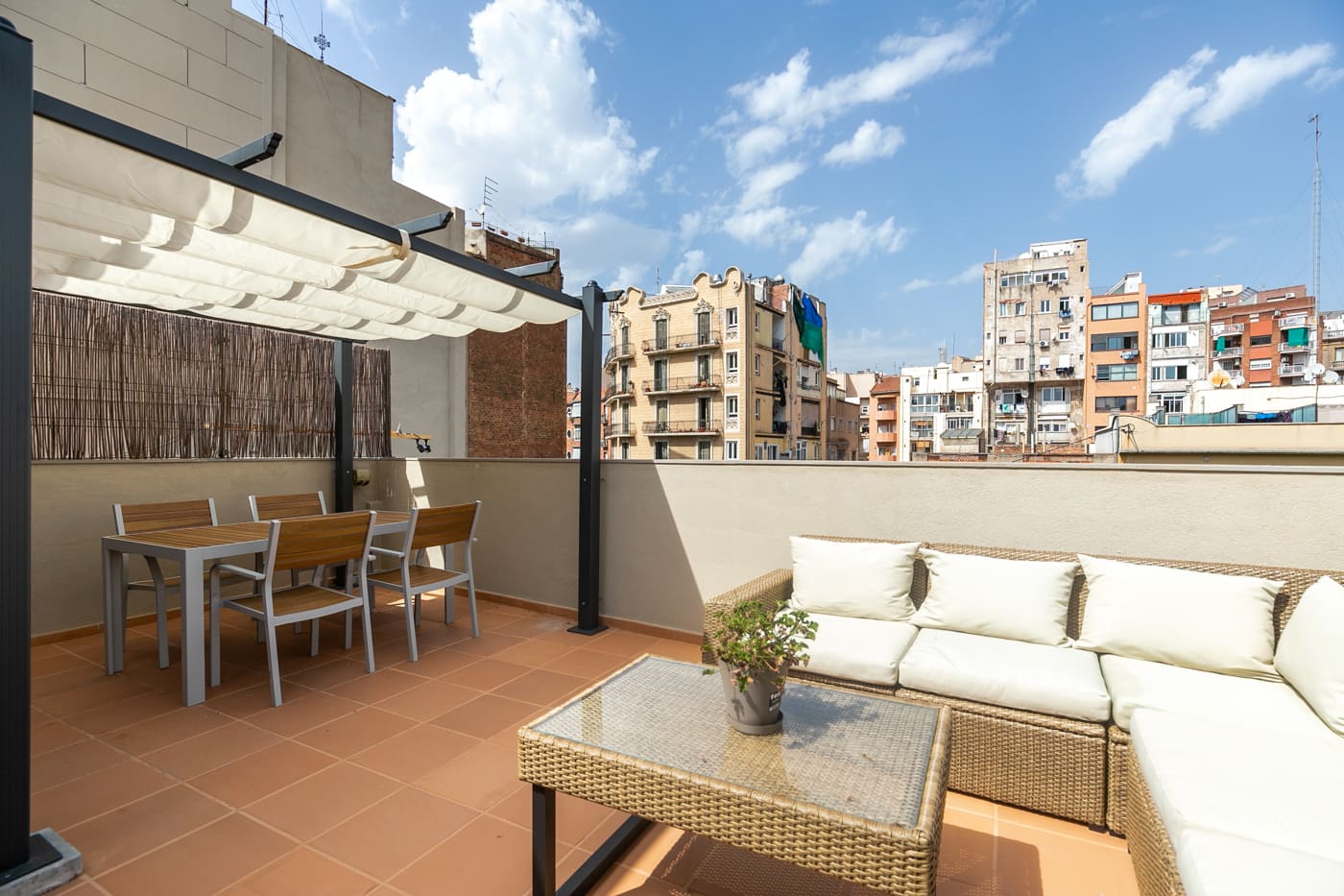 Terraza con pérgola de lona, mesa de exterior y sofá de fibra, sobre los tejados del barrio.