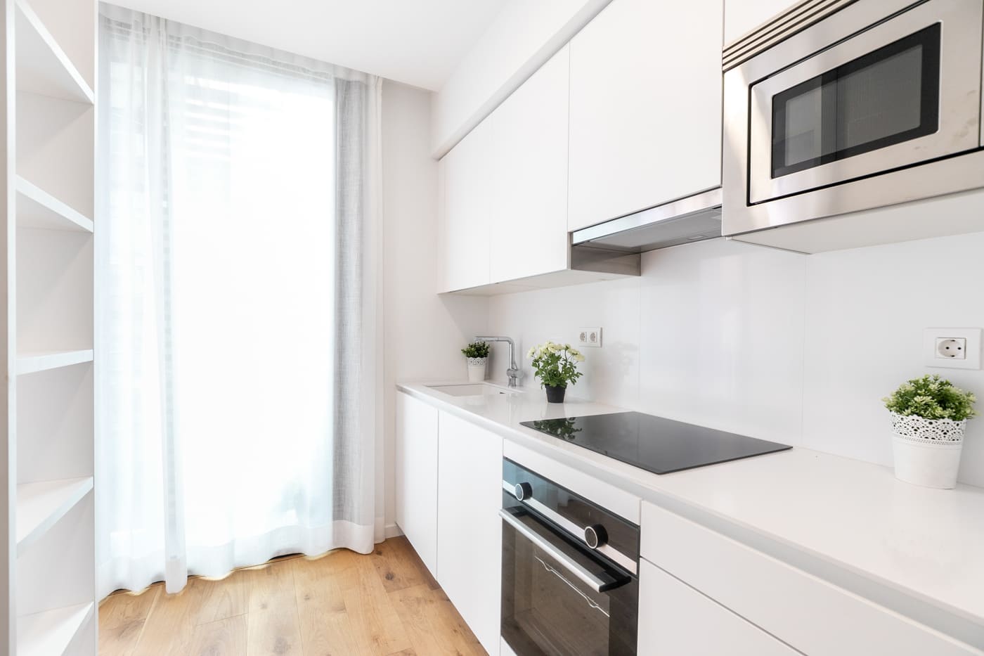 Cocina blanca en línea, sin tiradores, con encimera continua, horno y microondas integrados y salida a un patio.